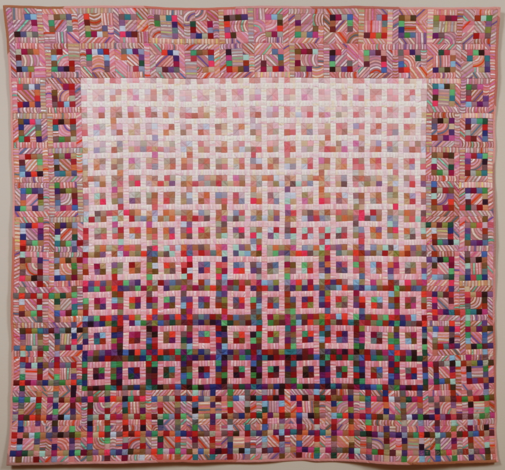 Quilt with repeating geometric pattern in pinks and reds.