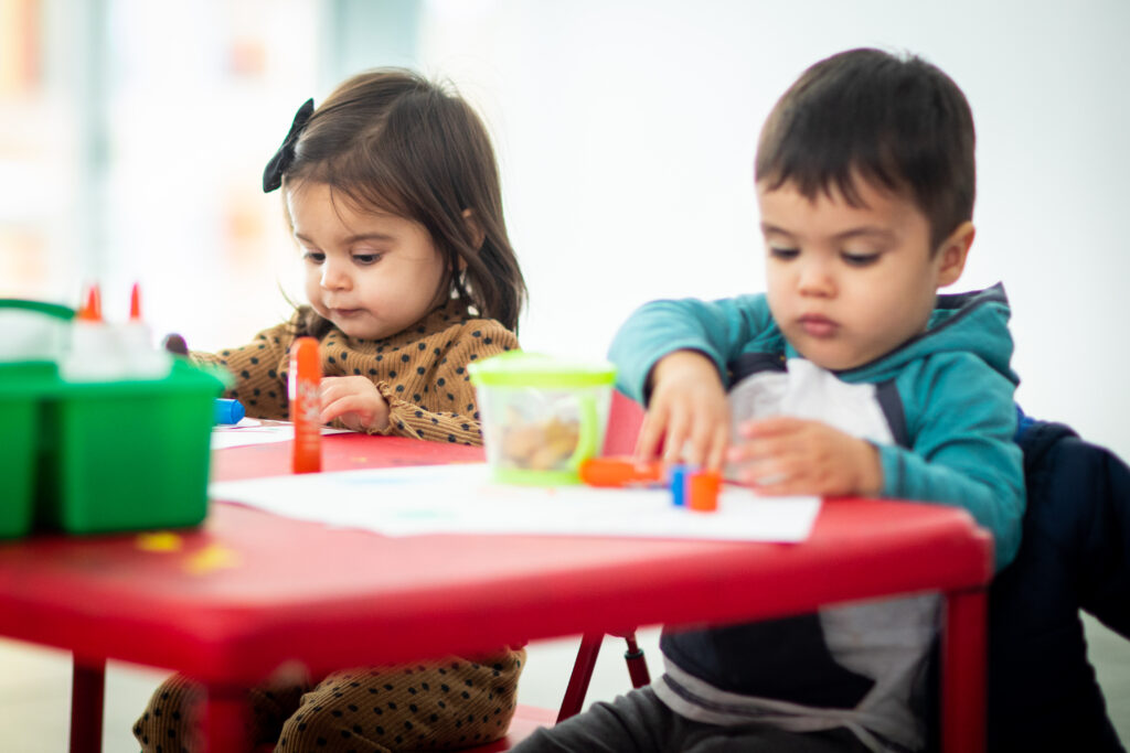 Aw Toddler saturday Jan2023 3 Two toddlers look down at a table while working on an art project