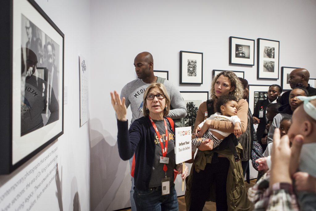 Photo of a teaching artist leading families and babies on an infant tour through a photography exhibition.