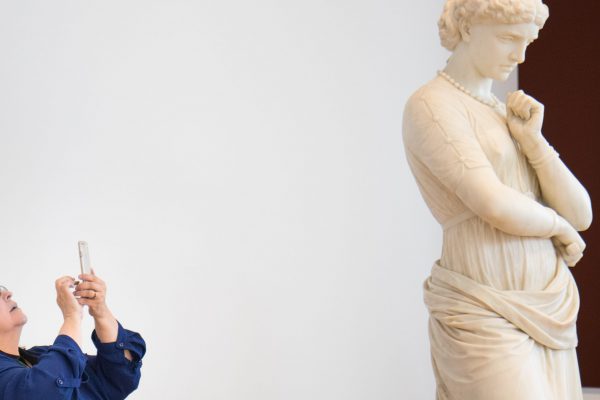 Woman taking a photograph of a marble statue using her phone